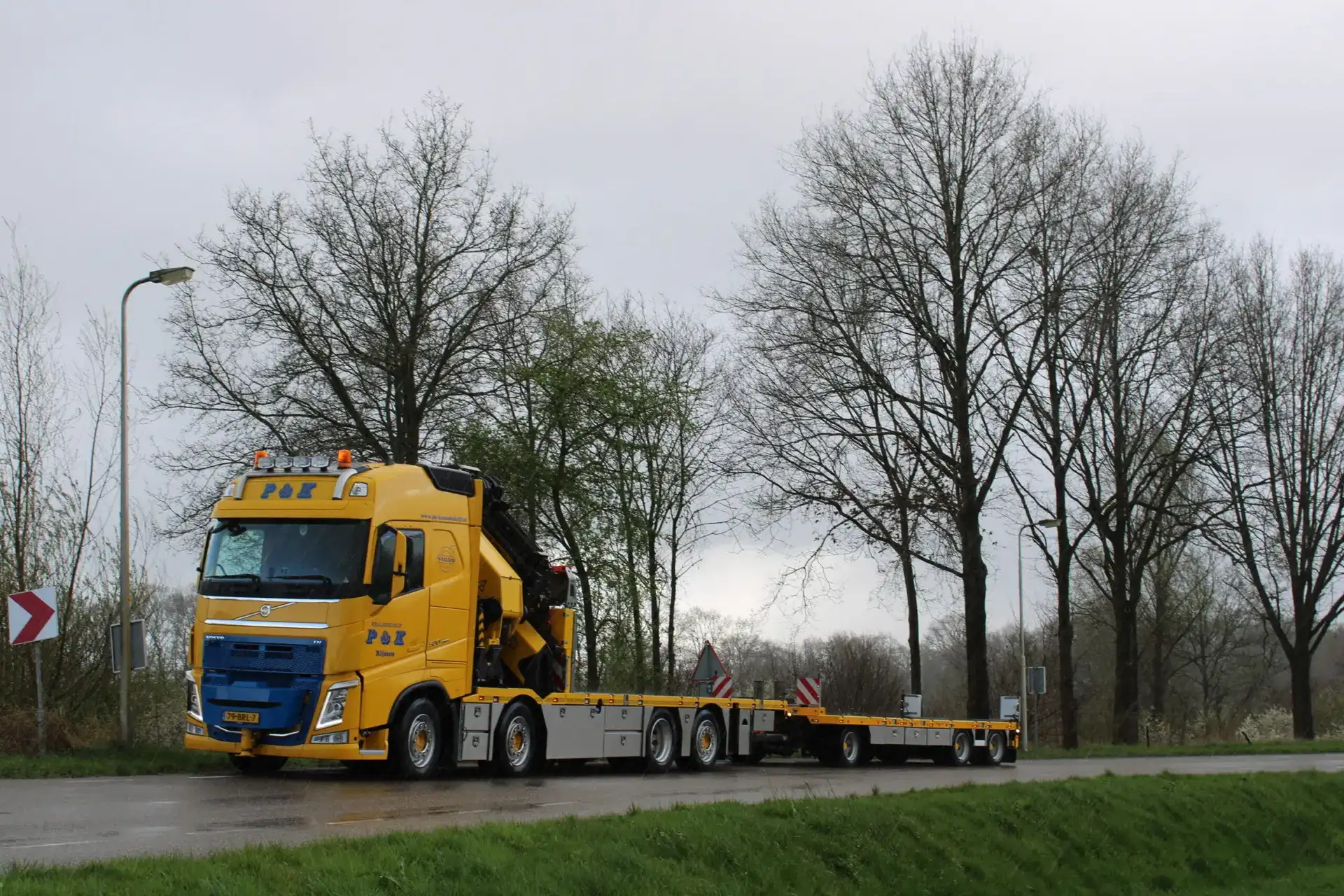 Sfeerfoto van een Autolaadkraan van P&K die op een weg rijdt met grijze wolken op de achtergrond