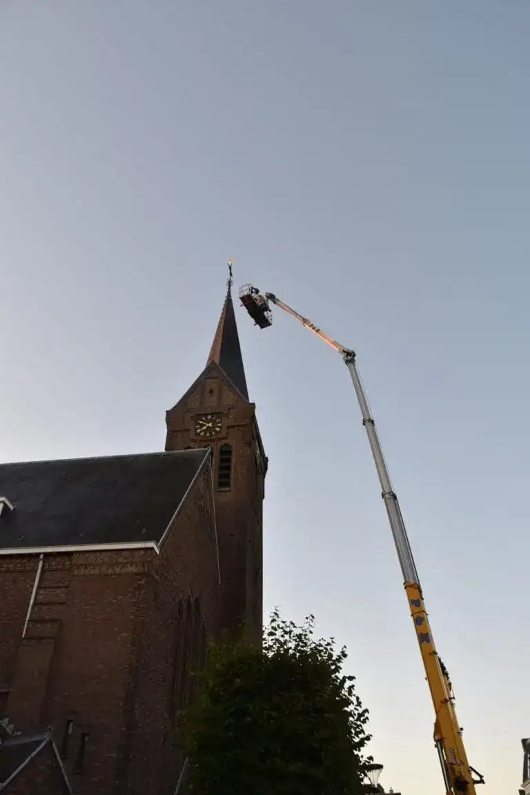 Autokraan met personenbak langs de spits van een kerktoren