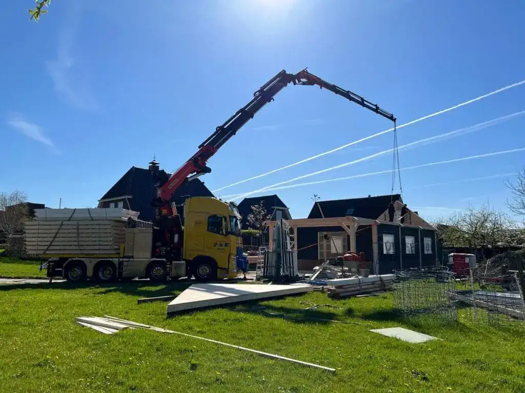 Vrachtwagen met autolaadkraan bij een woning in aanbouw