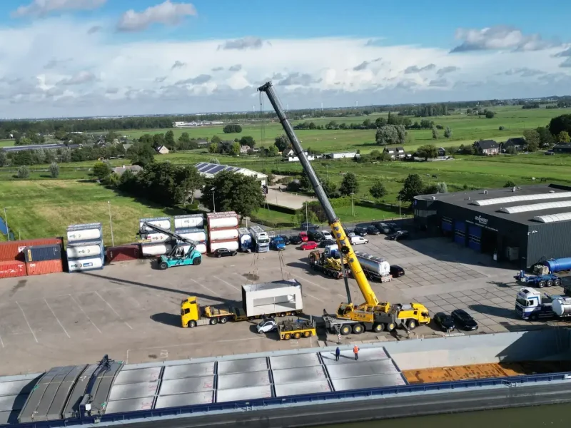 Dronefoto van het lossen van prefab garages met een kraan aan de waterkant