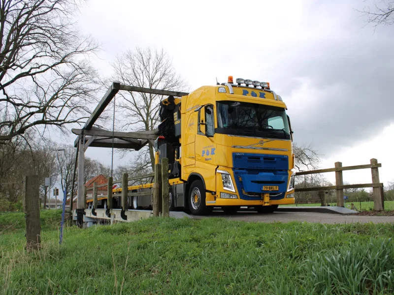 Sfeerfoto van een Autolaadkraan van P&K die over een kleine brug rijdt.